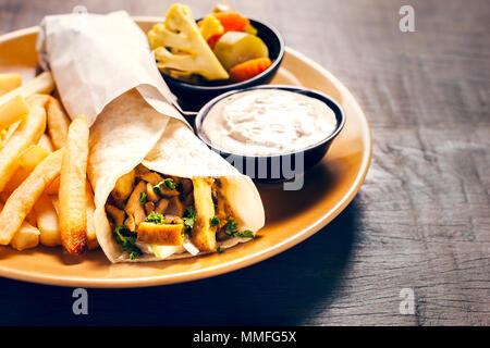 Griechische Gyros in pita Brot umwickelt. Mit Pommes frites serviert auf einem hölzernen Hintergrund Stockfoto