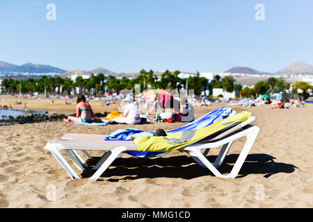 Sonnenliegen und Unerkennbare Personen Entspannen am Strand in Playa de Matagorda Puerto del Carmen, Lanzarote, Kanarische Inseln, Spanien Stockfoto