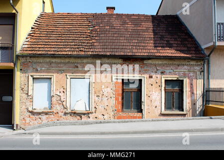 Kleine, angrenzende Haus durch shrapnels während des Krieges mit fallender Fassade beschädigt, beschädigte Dachziegel, fehlende Windows und sichtbaren Steine Stockfoto