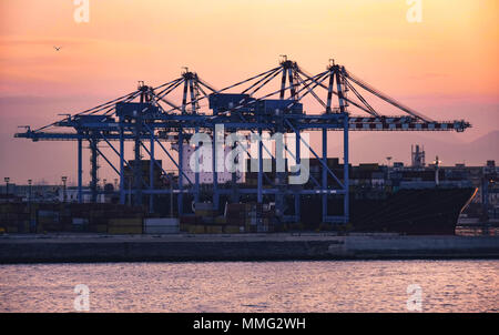 Hafen von Neapel in der Morgendämmerung vom Meer aus gesehen, die Kräne der Container auf Handelsschiffe zu heben vertäut an der Pier sind durch die ersten Sonnenstrahlen beleuchtet Stockfoto