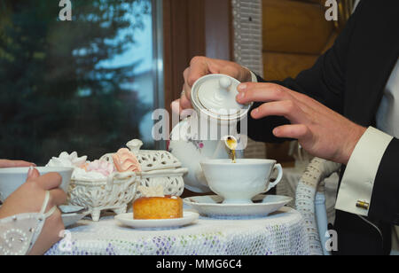 Der Bräutigam gießt Kaffee aus dem Wasserkocher in eine Schale. Sitzung mit der Braut im Cafe am Tisch Stockfoto