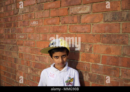 Pakistanische Junge in Batman Baseball Hut steht die Mauer, Rugby, England Stockfoto