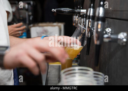 Nahaufnahme von einem Barkeeper Bier in Gießen eine Blondine in einem Kunststoff Glas mit Thema und tippen Sie auf den richtigen Fokus Stockfoto