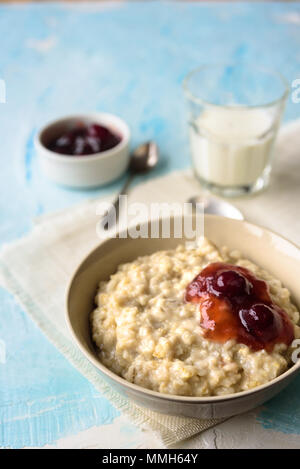 Haferflocken mit Butter und porrige Kirsche Konfitüre auf blauen Tabelle. Mit einem Glas Milch. Frühstück Stockfoto
