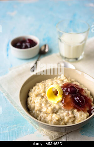 Haferflocken mit Butter und porrige Kirsche Konfitüre auf blauen Tabelle. Mit einem Glas Milch. Frühstück Stockfoto