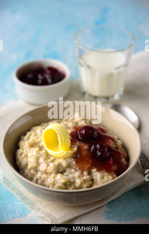 Haferflocken mit Butter und porrige Kirsche Konfitüre auf blauen Tabelle. Mit einem Glas Milch. Frühstück Stockfoto