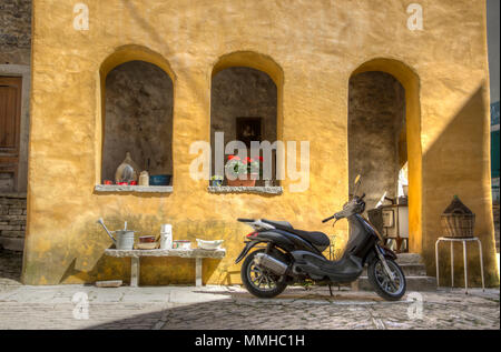 Istrien, Kroatien, April 2018 - Roller vor einem alten gelben Haus an der Ecke zweier Straßen geparkt in der antiken Stadt Oprtalj Stockfoto