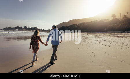 Ansicht der Rückseite des romantischen senior Paar hand in hand am Strand. Reifer Mann und Frau bei einem Spaziergang entlang der Küste. Stockfoto