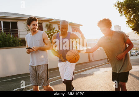 Drei basketball Männer auf der Straße Spielen mit dem Ball. Männer zu Fuß zurück nach einem Spiel der Basketball. Stockfoto