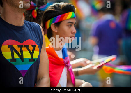 NEW YORK CITY - 25 Juni, 2017: Anhänger wave Regenbogen Fahnen und Verschleiß Herz NY t-shirt am Rande der Pride Parade in Greenwich Village. Stockfoto