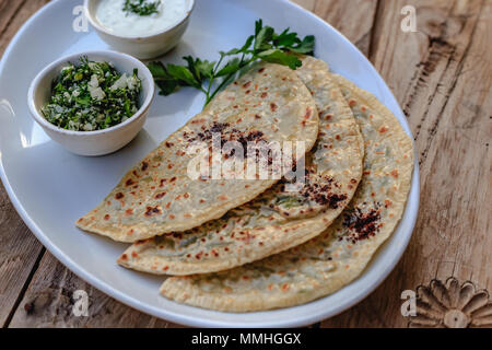 Traditionelle aserbaidschanische Küche. Qutabs Fladenbrot mit Grüns auf weißer Keramik Platte über der hölzernen Tischplatte. Horizontale Komposition. Stockfoto