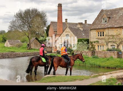 Reiter in einem Fluss Ford bei Lower Slaughter in den englischen Cotswolds mit Wassermühle im Hintergrund Stockfoto