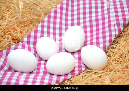 Weiße Eier mit Stroh auf einem karierten Tischtuch Stockfoto