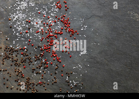 Rock mit Meersalz, braun und rosa Pfeffer auf schiefer Hintergrund mit Kopie Raum verstreut nach rechts Stockfoto