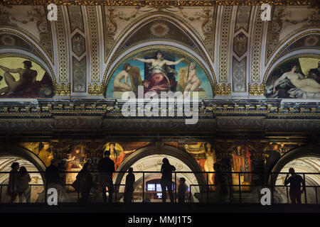 Besucher beobachten Wandmalereien der österreichische Maler Gustav Klimt vom Klimt Brücke (Klimtbrücke) temporäre Auf der Haupttreppe des Kunsthistorischen Museum (Museum für Kunstgeschichte) in Wien, Österreich installiert. Das Museum lädt die Besucher zu einer genaueren Betrachtung von Wandmalereien aus dem Jahr 1890 werden angezeigt 12 Meter über dem Boden an den 100. Todestag von Gustav Klimt 2018 zu markieren. Lünetten von österreichischen Maler Hans Makart sind oben gesehen. Stockfoto