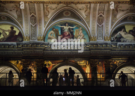 Besucher beobachten Wandmalereien der österreichische Maler Gustav Klimt vom Klimt Brücke (Klimtbrücke) temporäre Auf der Haupttreppe des Kunsthistorischen Museum (Museum für Kunstgeschichte) in Wien, Österreich installiert. Das Museum lädt die Besucher zu einer genaueren Betrachtung von Wandmalereien aus dem Jahr 1890 werden angezeigt 12 Meter über dem Boden an den 100. Todestag von Gustav Klimt 2018 zu markieren. Lünetten von österreichischen Maler Hans Makart sind oben gesehen. Stockfoto