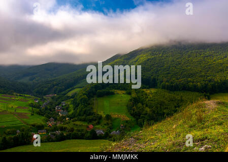 Kleine Karpaten Dorf in den Bergen. schöne Landschaft mit bewaldeten Hügeln und landwirtschaftlichen Feldern an einem bewölkten Morgen Stockfoto