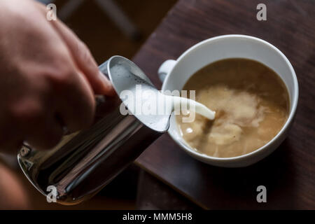 Man gießt in eine Tasse Kaffee mit Milch. Stockfoto