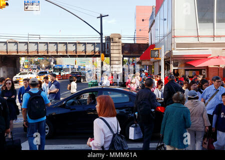 Ein Fahrer sitzt bei einem Handyanruf an einem Straßenübergang, während Fußgänger um das Fahrzeug in Downtown Flushing, New York, NY, 法拉盛華埠, 法拉盛 華裔美國人, 紐約 Stockfoto