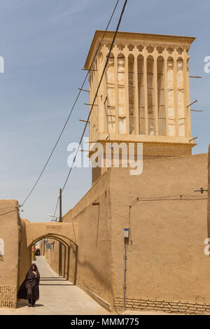 YAZD, IRAN - 27. APRIL 2015: Eine nicht identifizierte Frau geht durch die engen Straßen von Yazd im Iran Stockfoto