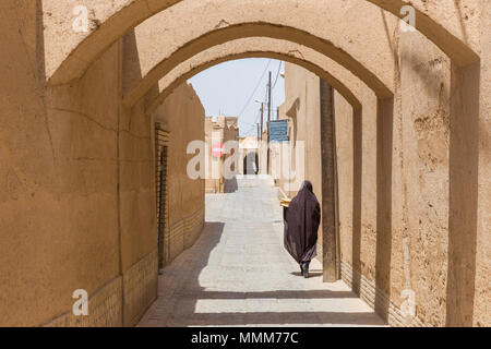 YAZD, IRAN - 27. APRIL 2015: Eine nicht identifizierte Frau geht durch die engen Straßen von Yazd im Iran Stockfoto