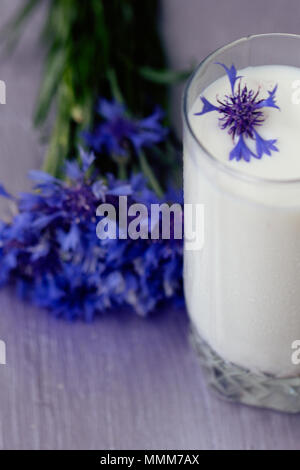 Glas Milch und ein Strauß Kornblumen auf einem Tisch in Lila Stockfoto