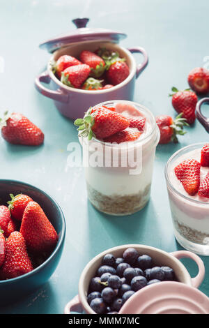 Strawberry cheesecake inside Glas Glas über einen blauen Hintergrund und den Blick von oben auf die Beeren, in Keramik farbige Cocotte, Heidelbeeren, Erdbeeren, ra Stockfoto