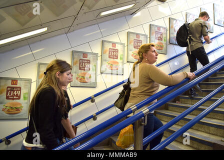 Menschen gehen vorbei Werbetafeln Förderung McDonalds BBQ Chicken Burger in der U-Bahn Station Oxford Circus in London. Junk Food ein Stockfoto