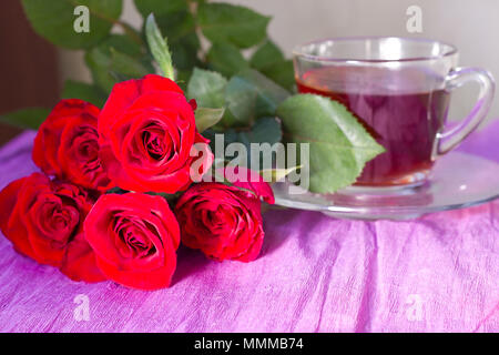 Strauß roter Rosen um Tassen Tee auf einem violetten Hintergrund Stockfoto