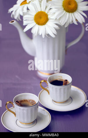 Schöne Kamille und Tasse Kaffee auf einem violetten Hintergrund Stockfoto