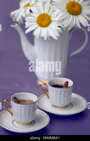 Schöne Kamille und Tasse Kaffee auf einem violetten Hintergrund Stockfoto