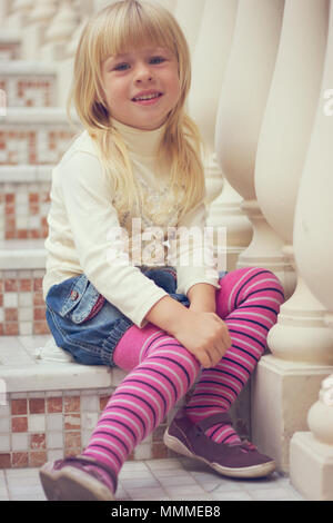 Mädchen 3 Jahre alt in einer Jeans Rock und rosa Strumpfhose sitzt auf einem wunderschönen Treppe Stockfoto
