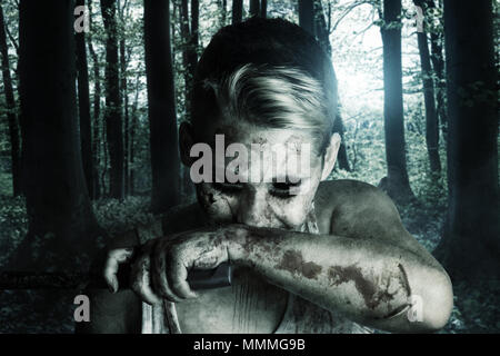 Portrait von Angry Blutsauger, der den Mund mit blutiger Hand und Messer vor der mystischen Wald wischen Stockfoto