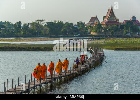 Maha Sarakham, Thailand - Dezember 20, 2015: Buddhistische Mönche marschieren Almosen zu suchen, während Händler zu Fuß waren auf Nakae Holzbrücke zu verkaufen in der Stockfoto