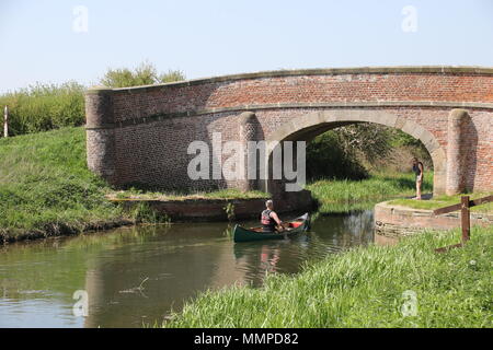 Eine Frau Uhren ein Mann in einem Kanu Paddel an einem Kanal bereit, unter einer Brücke zu gehen Stockfoto