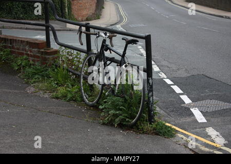 Ein Fahrrad lehnt, einsam an der Seite der Straße, Unkräuter durch die Speichen in einer Momentaufnahme des urbanen Lebens stoßen. Stockfoto