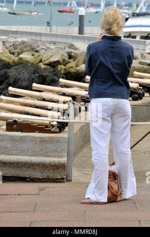 Eine Frau im Segelsport oder Bootfahren Stil Kleidung neben dem Royal Yacht Squadron startet Kanonen oder Kanonen während der Cowes Week auf der Insel Wight gekleidet. Stockfoto