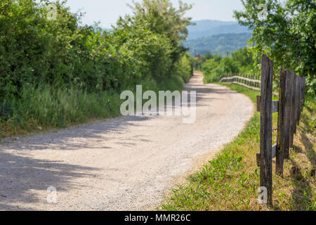 Landschaft Holzzaun Neben dem sandigen Weg und grüne Wälder Berge im Hintergrund. Stockfoto