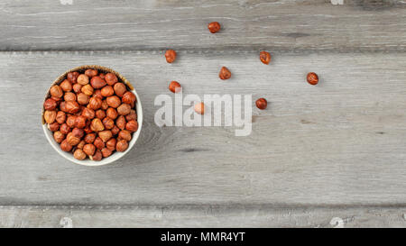 Tabelle der Ansicht von oben auf die kleine Schüssel voller Haselnüsse auf grau Holzschreibtisch. Stockfoto