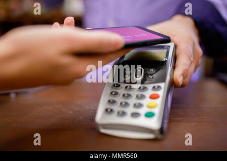 Foto des Verkäufers mit Terminal und Käufer mit Smartphone in Store Stockfoto