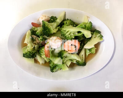 Gebratener Brokkoli mit Garnelen, ein einfaches asiatisches Fischgericht, das auf einem weißen Teller serviert wird. Stockfoto