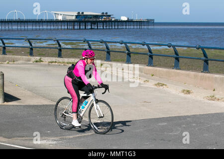 Mollige Frau, die in leuchtendem rosa Outfit in Southport, Merseyside, Großbritannien, radelt 13/05/2018. Wetter in Großbritannien. Sonniger Tag an der Küste, da die Temperaturen im Nordwesten voraussichtlich steigen werden. Zu Beginn des Tages können die Bewohner des Resorts an der Strandpromenade leichte Morgenübungen machen. Quelle: MediaWorldImages/AlamyLiveNews Stockfoto