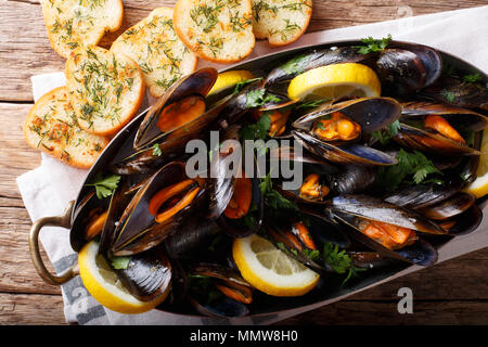 Französische Miesmuscheln mit Zitrone, Petersilie und Knoblauch close-up, das in einem Kupfertopf und Toast auf dem Tisch. horizontal oben Ansicht von oben Stockfoto