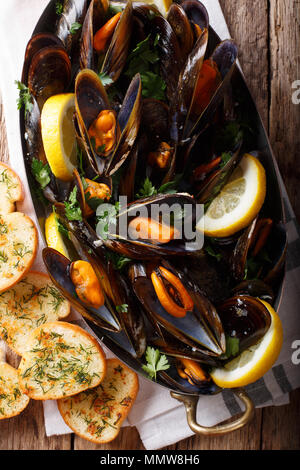 Französische Miesmuscheln mit Zitrone, Petersilie und Knoblauch close-up, das in einem Kupfertopf und Toast auf dem Tisch. Vertikal oben Ansicht von oben Stockfoto