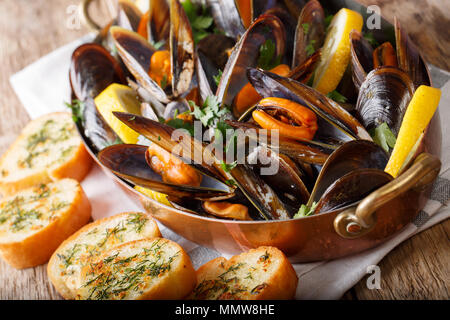 Gekochte Miesmuscheln mit Zitrone, Petersilie und Knoblauch Makro in einem Topf auf einem Tisch. Horizontale Stockfoto