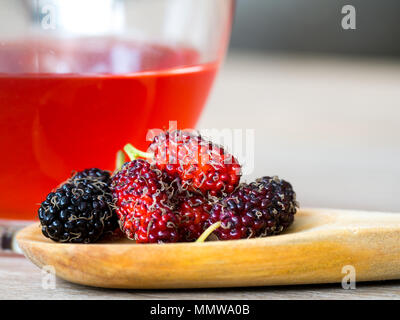 Close up Gruppe von maulbeeren ist auf einem hölzernen Löffel vor einem Glas maulbeeren Wasser gestellt. Mulberry diese eine Frucht und gegessen werden kann. Mulberry ist Stockfoto