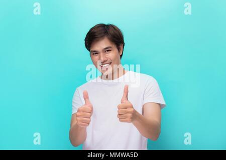 Portrait eines glücklichen jungen Mann mit Daumen nach oben Geste über graue Wand isoliert Stockfoto