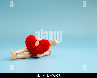 Hölzerne Marionette umarmen Rotes Herz und fallen auf den Boden. Kopieren Sie Platz für Text und Inhalt. Konzept der Liebe und Herzinfarkt und gesundheitliche Probleme Stockfoto