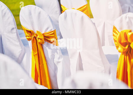 Eine Gruppe von Weißen spendex Stühle mit Gold organza flügel Dekoration während der Hochzeit am Strand Ort der Vorbereitung für Hochzeit Stockfoto