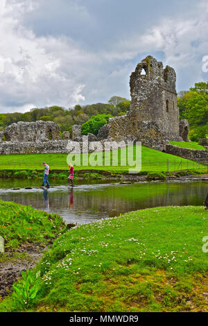 Ein junges Paar vorsichtig die berühmten trittsteine Überqueren sie den Fluss, wo es vergeht Ewenny Ogmore Schloss, nr Bridgend, South Wales Stockfoto